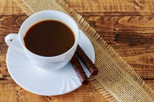 caffè tazza e fagioli, cannella bastoni, cioccolato su di legno tavolo sfondo foto