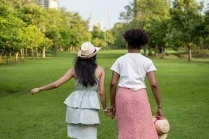 diversità di LGBTQ lesbica coppia è rilassante Tenere loro mano insieme nel pubblico parco durante estate stagione per godere il tempo libero tempo per In arrivo su di guardaroba e inclusione foto