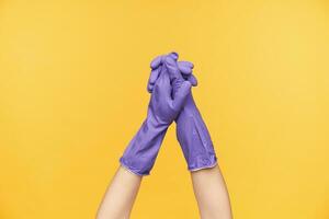 studio foto di giovane femmina mani nel viola gomma da cancellare guanti tremante ogni altro mentre in posa al di sopra di giallo sfondo, donna è andando per pulito il Casa