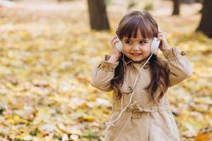 bambina che ascolta musica con le cuffie nel parco autunnale foto