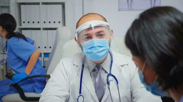 vicino su di medico con visiera A proposito di con donna nel medico ufficio durante covid19. medico specialista nel medicina fornire Salute cura Servizi consultazione trattamento visita medica nel ospedale foto