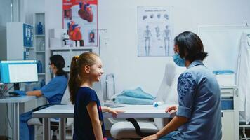 madre e figlia parlando e in attesa per il medico nel medico ufficio durante coronavirus. specialista nel medicina con protezione maschera fornire Salute Servizi, consultazione, trattamento nel Ospedale. foto