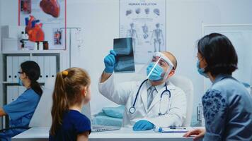 medico lavoratore con protezione maschera spiegando raggi X di genitore durante coronavirus. specialista nel medicina fornire Salute cura Servizi consultazione, radiografico trattamento nel clinica Consiglio dei ministri ospedale foto