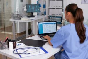 medico infermiera controllo paziente documentazione su il computer portatile nel ospedale ufficio. Salute cura medico utilizzando computer nel moderno clinica guardare a tenere sotto controllo, medicinale, professione, scrub. foto