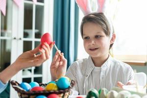 ragazzo carino e sorridente con orecchie da coniglio carine dipinge un uovo di Pasqua. foto