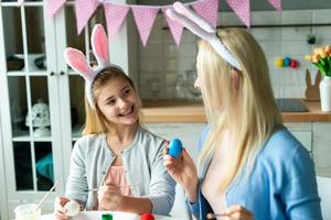 primo piano della figlia sorridente che guarda la mamma che sta dipingendo l'uovo di pasqua. foto