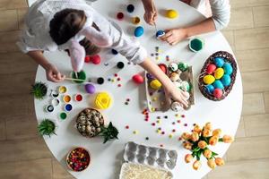 vista dall'alto, i bambini al tavolo dipingono le uova di Pasqua, le vernici, l'atmosfera di lavoro. foto