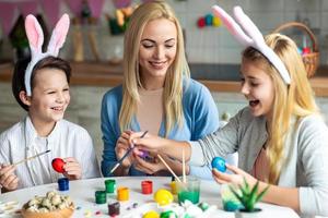 madre felice che si diverte con i suoi bambini mentre colora le uova di Pasqua