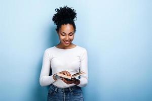 attraente, giovane donna con un sorriso legge un libro interessante su uno sfondo di muro blu foto