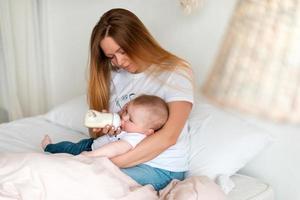 una giovane e bella madre dà al suo bambino la pappa da una bottiglia foto