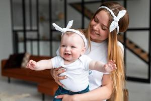 donna felice e sorridente che tiene in braccio una figlia piccola e bella nell'appartamento foto