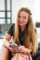 bella e attraente ragazza seduta sul divano con un telefono in mano, distogliendo lo sguardo foto