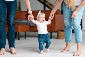 i genitori tengono una bambina carina per le maniglie, le insegnano a camminare foto