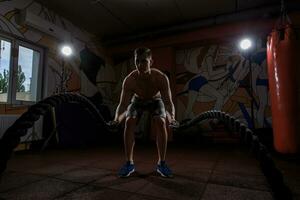 giovane uomo Lavorando su con battaglia corde a CrossFit Palestra foto