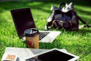 il computer portatile computer su verde erba con caffè tazza, Borsa e tavoletta nel all'aperto parco foto