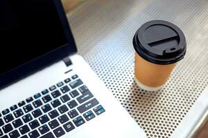 modello Immagine di il computer portatile con vuoto nero schermo e caffè tazza su metallo panchina nel natura all'aperto parco foto