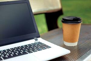 modello Immagine di il computer portatile con vuoto nero schermo e caffè tazza su metallo panchina nel natura all'aperto parco foto