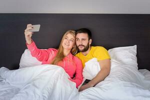 giovane contento coppia su letto fare autoscatto con telefono telecamera. foto