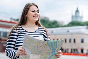 giovane donna vestita con un maglione a righe, con una mappa in mano, all'aperto, cammina per le strade della città foto