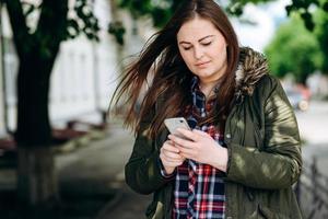 concentrata, bella ragazza che guarda qualcosa al telefono, all'aperto foto