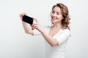 la ragazza sorridente sullo sfondo del muro bianco fa selfie sul telefono foto
