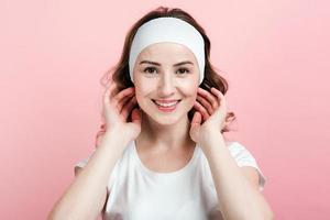 onestamente sorridente giovane donna in una fasciatura per capelli in posa su uno sfondo rosa foto