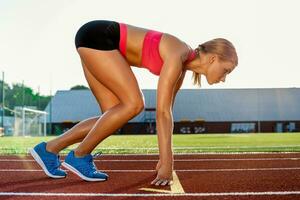 giovane donna atleta a di partenza posizione pronto per inizio un' gara su pista. foto