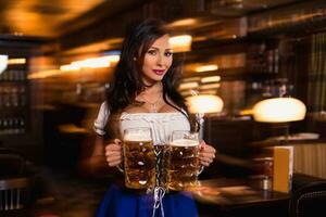 bellissimo femmina cameriera indossare tradizionale dirndl e Tenere enorme birre nel un' pub. foto