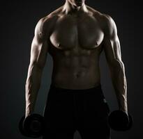 muscolare uomo mostrando Perfetto corpo con manubri su nero sfondo foto