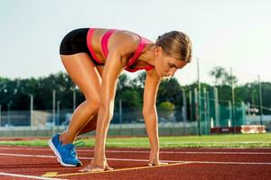 giovane donna atleta a di partenza posizione pronto per inizio un' gara su pista. foto