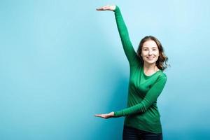 carina ragazza bionda che indossa un maglione verde che mostra uno spazio di copia con le mani su sfondo blu foto