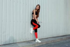 femmina atleta potabile acqua mentre in piedi di un' grigio parete. foto