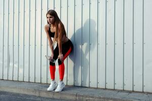 femmina atleta potabile acqua mentre in piedi di un' grigio parete. foto