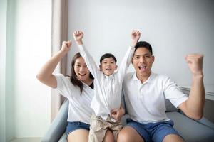 famiglia eccitata e felice con le braccia alzate mentre si guarda la televisione a casa foto