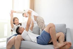 famiglia asiatica felice con il figlio a casa sul divano che gioca e ride foto