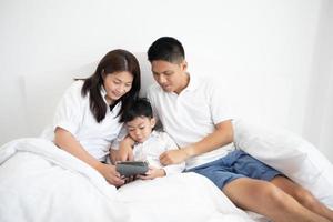 famiglia e figlio che guardano e giocano al tablet sul letto foto