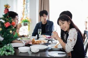 cena con un gruppo asiatico di migliori amici che si godono un drink serale seduti al tavolo da pranzo in cucina insieme, soft focus foto