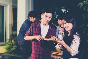 gruppo asiatico di amici che hanno barbecue in giardino all'aperto che ridono con bevande alcoliche di birra la notte? foto