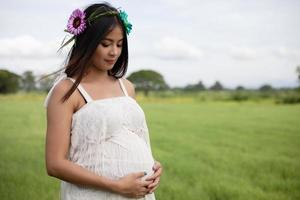 donna asiatica incinta felice e orgogliosa che guarda la sua pancia in un parco all'alba