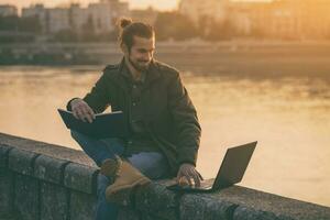 bello uomo d'affari utilizzando personale organizzatore e il computer portatile mentre seduta di il fiume.tonico Immagine foto