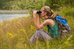 donna escursionista utilizzando binocolo mentre la spesa tempo nel il bellissimo natura. foto