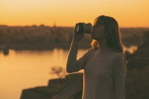 silhouette di un' donna potabile caffè a il tramonto. foto