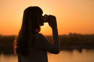 silhouette di un' donna potabile caffè a il tramonto. foto