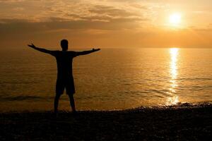 silhouette di un' uomo saluto il tramonto a il mare foto