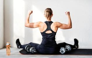 vista posteriore della giovane donna bionda che si allena con i manubri che mostrano i muscoli della schiena e delle braccia foto