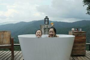 asiatico famiglia, mamma e bambino giocando insieme, senza fretta rilassare nel vasca da bagno, godere felicemente con panoramico montagna gamma Visualizza di tropicale paesaggio nel naturale scenario viaggio ricorrere per vacanza vacanza. foto