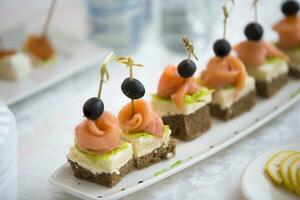 buffet piatti.crostini su un' bianca piatto. piccolo panini su un' bastone. merenda di nero pane, salmone e insalata foto