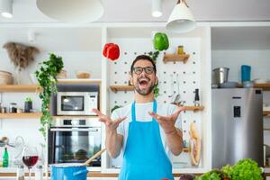 allegro giovane uomo lanciare verdure nel aria a il cucina foto