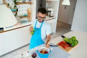 contento sorridente uomo preparazione gustoso pasto. giovane uomo cucinando nel il cucina. foto