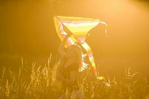 contento giovane donna in esecuzione con un' aquilone su un' radura a tramonto nel estate foto